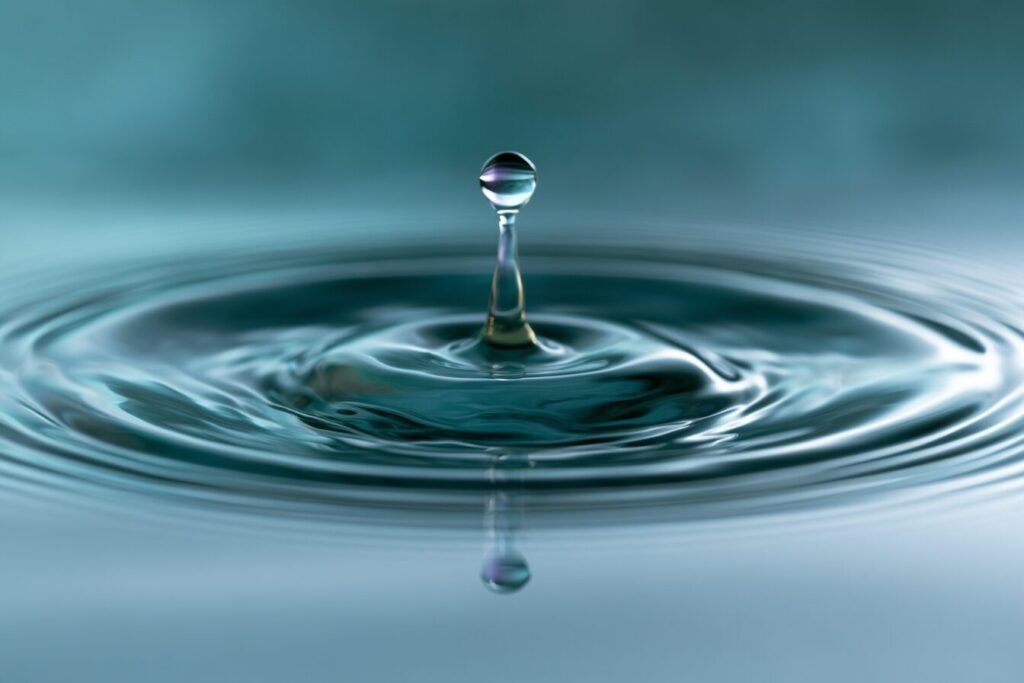 Macro photograph of a water droplet rebounding above teal ripples